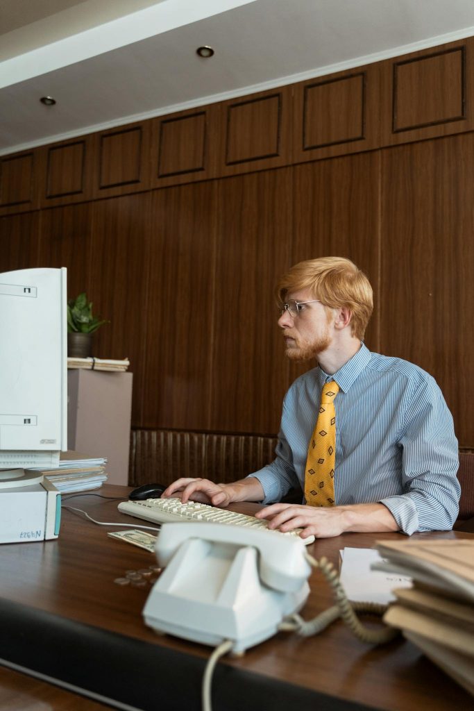 Businessman in vintage office setting, focused on computer work, dressed in retro attire.